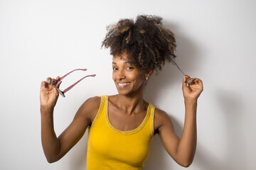 Young black casual woman holding her eye glasses. Afro hairstyle happy model against blank white wall. - 666668612