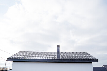 The roof of a country house, the heating hood pipe stands on the roof, gray corrugated sheeting covers the house from above, a new house.