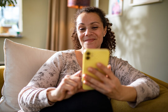 Happy Hispanic woman using the smartphone at home