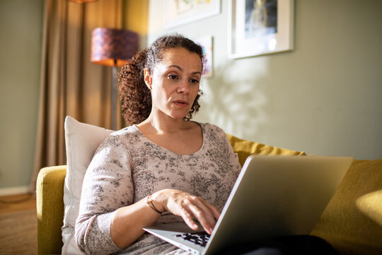 Hispanic woman using the laptop on the couch at home