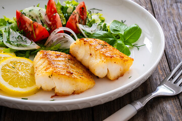 Seared cod loin and fresh vegetables on wooden table
