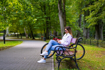 Beautiful woman resting on bench in city park using mobile phone
