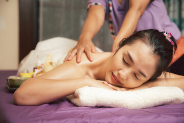 Asian woman enjoying back and arm massage with essential oil in massage spa salon. Young girl in spa massage. Healthy treatment concept.