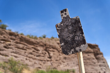 Weathered tactical AR500 Steel silhouette targets with sitting on wood stands at desert outdoor range in summer.
