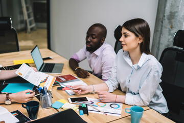 Creative multiethnic students arguing documents together at office