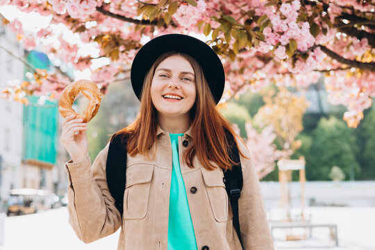 Attractive young female tourist is holding prezel, traditional polish bagel near Wawel castle, in Krakow. Traveling Europe in spring. High quality photo