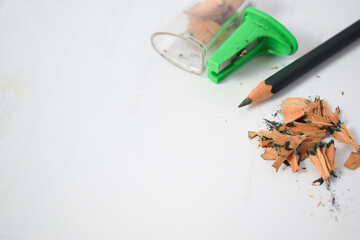 green pencil sharpener and dark green pencils, pencil shavings on white background