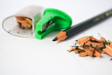 green pencil sharpener and dark green pencils, pencil shavings on white background