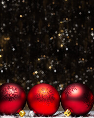Christmas decorations composition view of three red evening balls with red glitter snowflakes on it on dark background with silver and gold colors bokeh. Holiday concept with copy space on top.