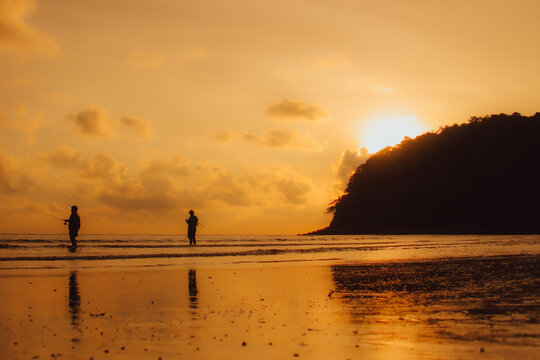 Layan Beach, Phuket, Thailand,Silhouette Two Asians standing fishing at the sea as the sun sets,