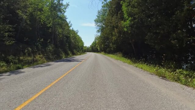 Front view forward driving Plate on a Highway 551. POV driving car view. Rural winding road with tree lined forest. Sunny afternoon blue sky. Curved road ahead on Manitoulin Island.