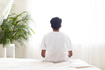 Loneliness. Rear View Of Male Sitting On Bed And Looking At Window