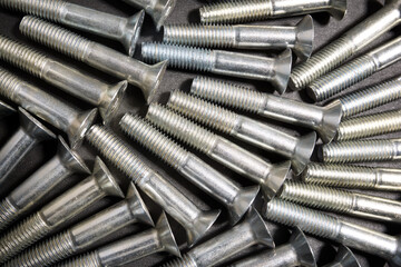 Group of countersunk head metal fastening screws on a table.