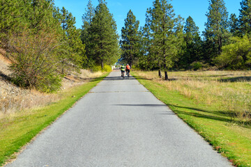 Obraz premium Two bicyclists ride their bikes along the Centennial Trail near the Idaho Washington border in the rural city of Post Falls, Idaho, a suburb of the Spokane and Coeur d'alene general areas.