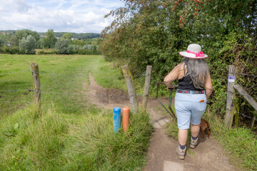 Mature hiker walking in Epen Bronnenland nature reserve, poles with different hiking routes, blue, orange and purple, countryside in background, sunny day in Gulpen-Wittem, South Limburg, Netherlands