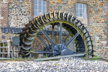 Old Eper or Wingbergermolen water mill on Geul river, stone wall with two windows, with its support, rotating wheel, shaft and blades, sunny day at Terpoorterweg, Epen, South Limburg, Netherlands