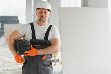 A man with a beard in a helmet and work clothes. Portrait of a worker in workwear with copy space.