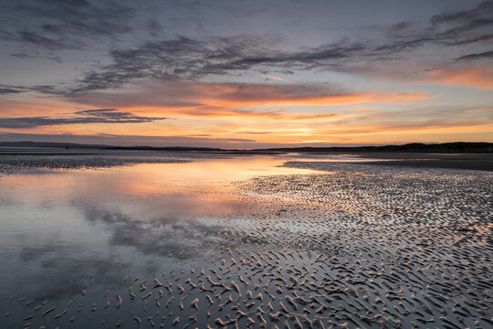 Sunset reflections on sandy beach at sunset, Camber Sands, East Sussex, England