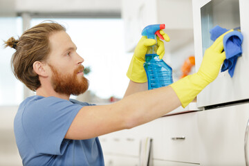 man spraying an oven in kitchen