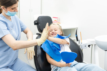 Little patient girl sitting in a chair gives a high five to a pediatric dentist after dental...