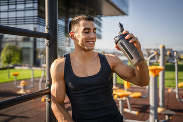 One caucasian man young male athlete take a brake during outdoor training in the park outdoor gym hold supplement shaker in hand happy confident strong copy space