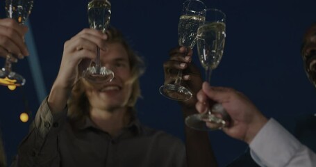 Multi-ethnic group of colleagues clinking champagne glasses celebrating promotion at corporate party at night outdoors on rooftop. Team and leisure activity concept.