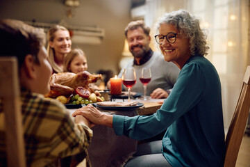 Happy senior woman communicating with her grandson during family meal at dining table on Thanksgiving.