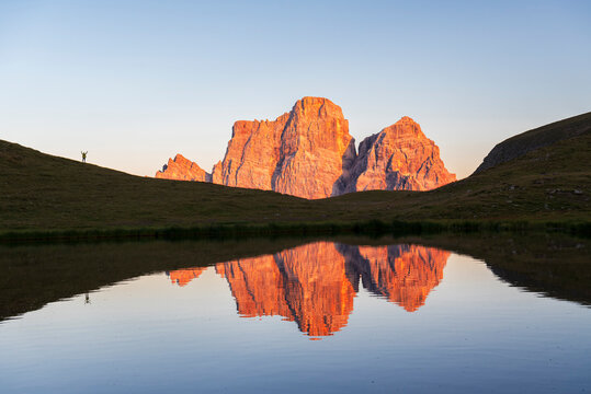 Hiker admires the sunset in front of the giant massif of Pelmo mountain reflected in the water of the small lake of Baste, Giau Pass, Cortina d'Ampezzo, Dolomites of Belluno, Veneto