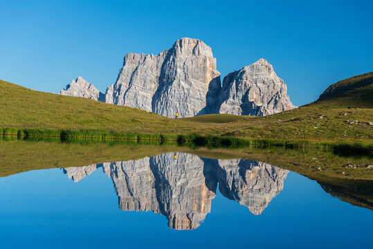 Hiker and Mount Pelmo reflected in the water of Baste Lake on a sunny day, Belluno Dolomites, Belluno province, Veneto