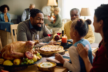 Happy black father talks to his daughter during Thanksgiving family meal at dining table.