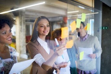 Business people putting sticky notes on a glass board in a modern office