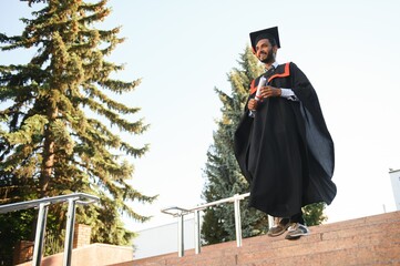 Portrait of indian handsome male graduate in graduation robe.