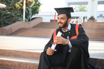 Handsome indian graduate in graduation glow with diploma.