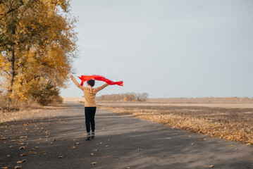 A little boy is holding the flag of Poland in nature. A child runs along the road with a flickering national flag in his hands. Concept of national holidays and patriotic events. Independence Day