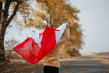 A little boy is holding the flag of Poland in nature. A child runs along the road with a flickering national flag in his hands. Concept of national holidays and patriotic events. Independence Day