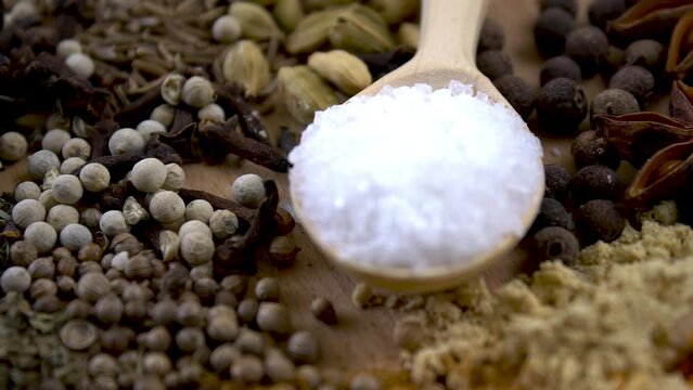 Close-up. Large sea salt in a wooden spoon. Various spices and salt crystals. Black pepper, cumin, coriander, turmeric, salt. Coarse salt for marinating.