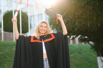 Portrait enthusiastic female college student graduate in cap and gown celebrating, holding diploma.