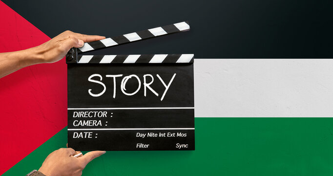 The hands of the camera crew in the film industry holding a black film slate or Clapperboard Write the word "story" with white chalk on top of a Palestine flag in concrete texture