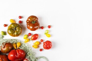 Red, green, yellow and striped tomatoes in a string bag on a gray table with space for text. Flat lay. Healthy food, fresh healthy vegetables from the garden