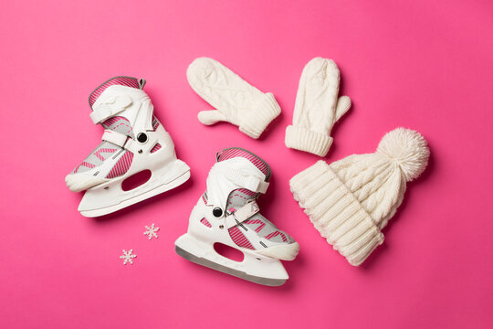 Ice skates and knitted hat on color background, top view