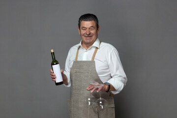Mature man with two glasses and a bottle of wine on a gray background, studio.