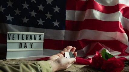hand of military man holding his dog tag near a USA flag 