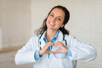 Joyful doctor making heart shape with hands, smiling at camera - obrazy, fototapety, plakaty