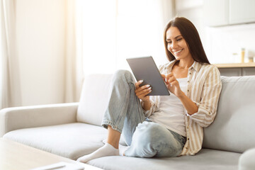 Smiling beautiful woman relaxing with digital tablet on couch at home