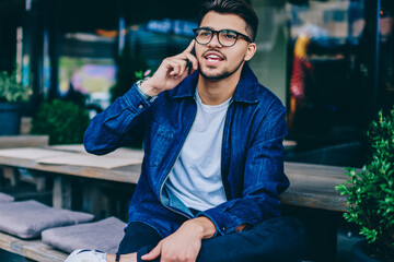 Smiling caucasian male in casual wear making booking by telephone call while sitting at cafe terrace