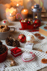 Various colorful Christmas decorations, soft blanket, cup of tea, sweet snacks and lit candles on the table. Cozy Christmas atmosphere at home. Selective focus.