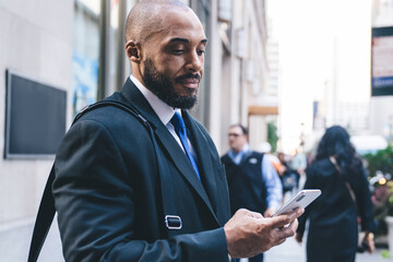 Naklejka na ściany i meble Black businessman using smartphone on street