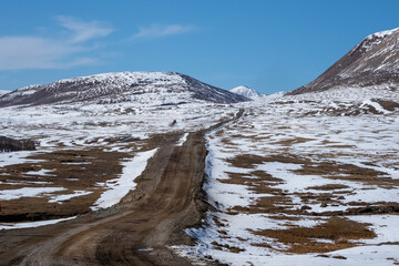 Mountain track off-road to a high-mountain village. Snow-covered narrow mountain road on the slope of snow mountains. Dangerous off-road driving along the mountains to the edge and steep cliffs.