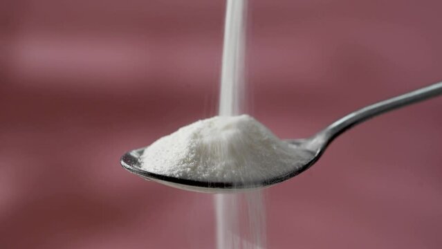 Collagen protein powder pouring in a spoon, pink background. Food beauty and health supplement