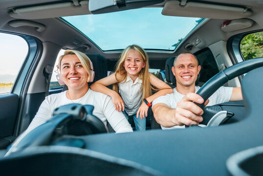 Happy young couple with daughter inside the modern car with panoramic roof during auto trop. They are smiling, laughing during road trip. Family values, traveling concepts.